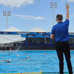 árbitro de polo aquático com o braço erguido em frente a uma piscina