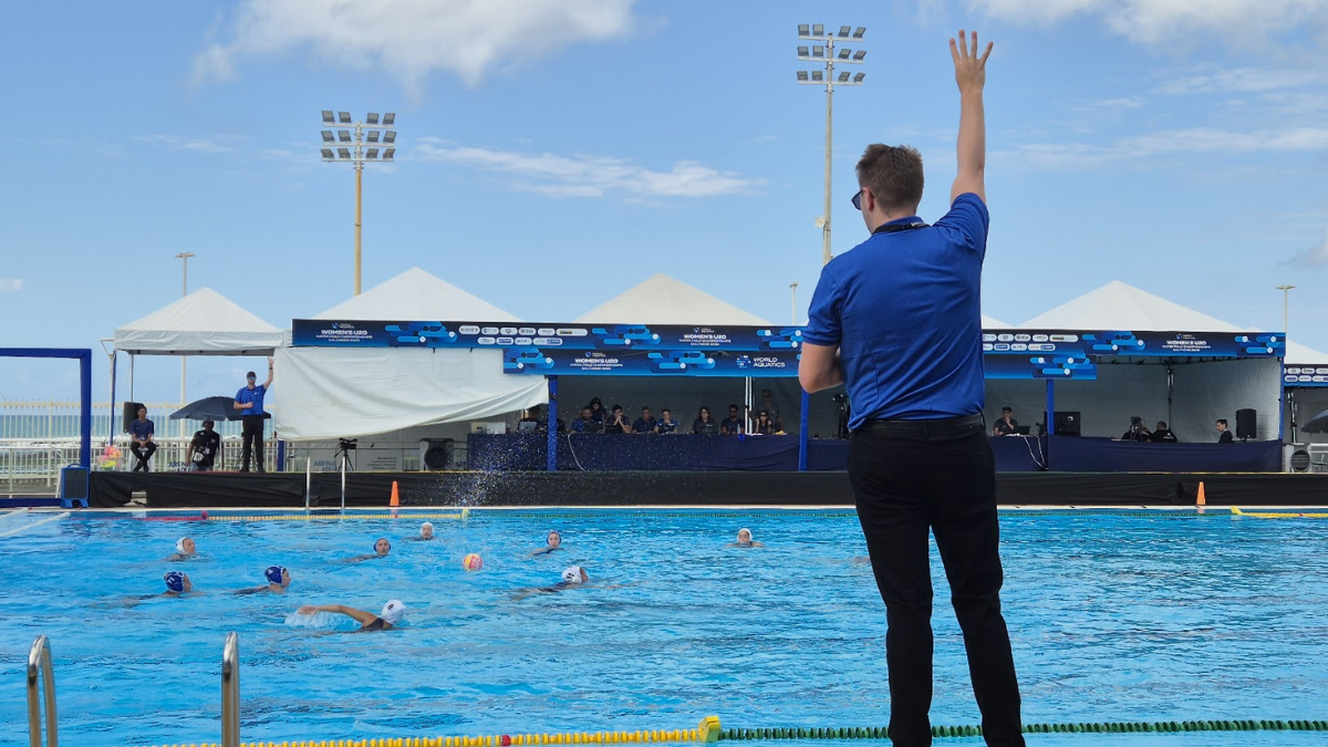 árbitro de polo aquático com o braço erguido em frente a uma piscina