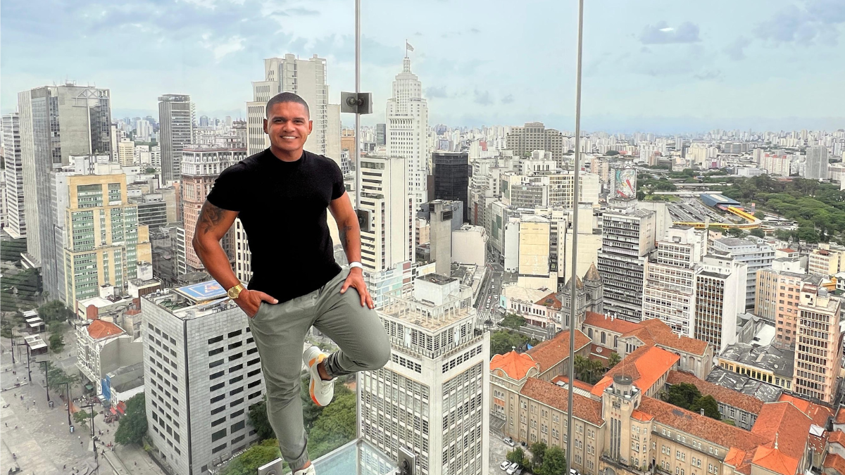 empresário Adriano de Barros numa sacada transparente com paisagem urbana ao fundo