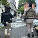um policial civil e um militar andando lado a lado numa comunidade.