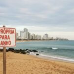 praia vazia com placa escrito "imprópria para banho"
