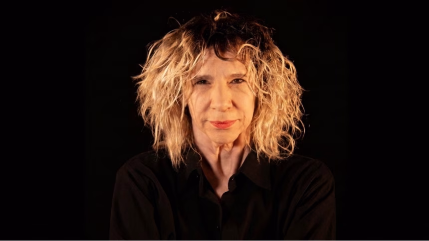 dramaturga Denise Stoklos olhando a câmera sobre fundo preto
